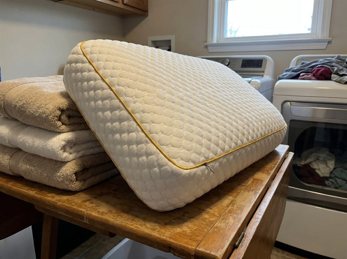 Freshly laundered Pillowash washable pillow on a wooden table beside a stack of folded towels in a laundry room