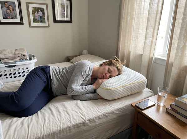 A mother naps on her side with her head on a Pillowash washable pillow, folded laundry and family photos behind her