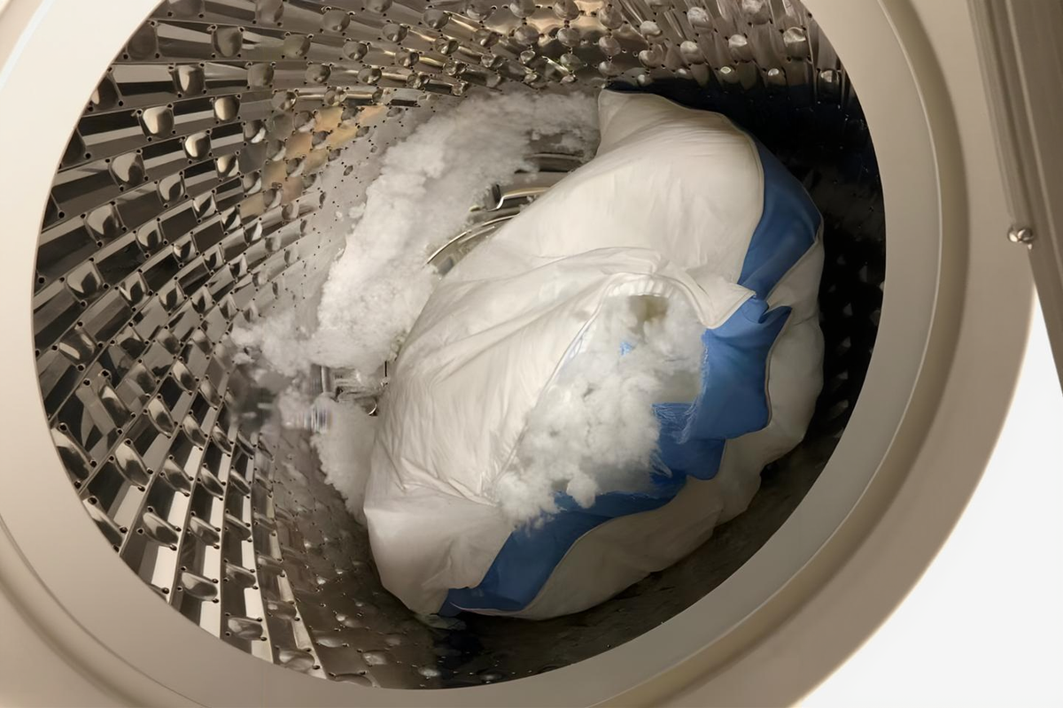 An ordinary pillow burst open in the washing machine, its fibre fill spilling into the drum