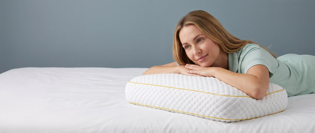 A woman lying on a white bed with her arms folded over a Pillowash washable pillow, resting her cheek on her hands