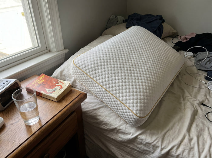 Pillowash washable pillow on a bed next to a nightstand holding a paperback book and a glass of water