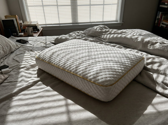 Pillowash washable pillow on a rumpled bed with striped morning shadows cast by window blinds